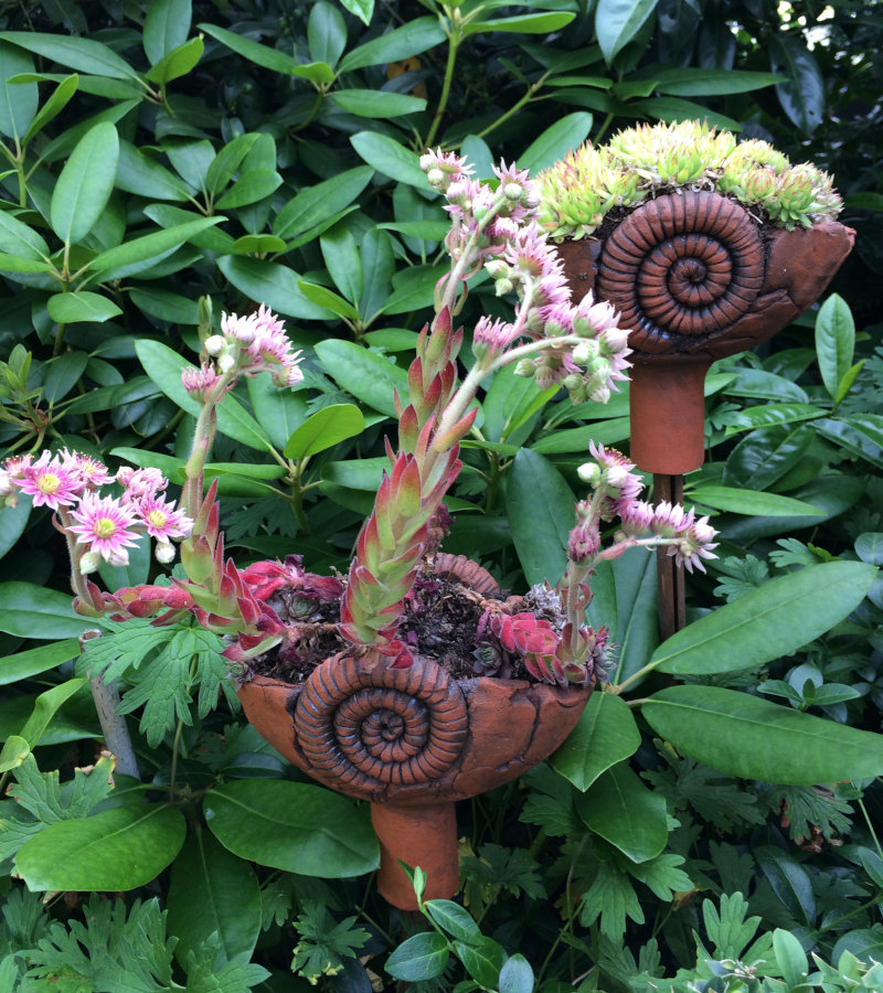 Gartenstecker aus roter Keramik vor Rhododendron